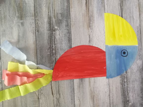 dwie części talerzyka połączone tworzą kształt papugi, jako ogon przyklejone są kolorowe paski bibuły